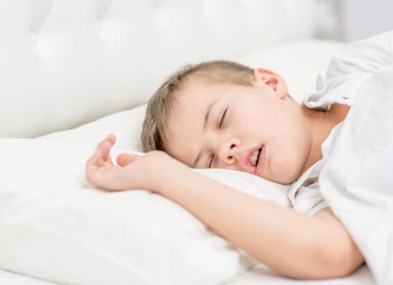 Young boy sleeping with his mouth open on a white pillow, showing signs of mouth breathing